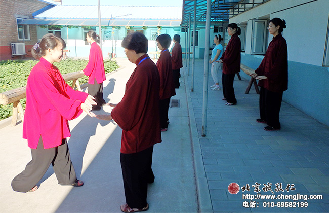 清晨陽光明媚，紅衣綠葉藍天；專業太極拳老師認真指導學員太極定式練習。